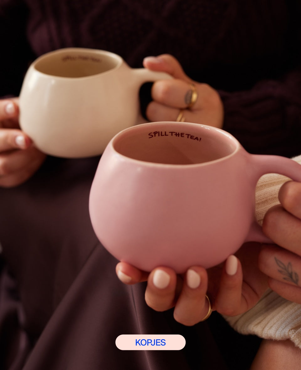 Zwei Personen halten Tassen mit der Aufschrift "SPILL THE TEA", eine rosa und eine weiße, in den Händen.