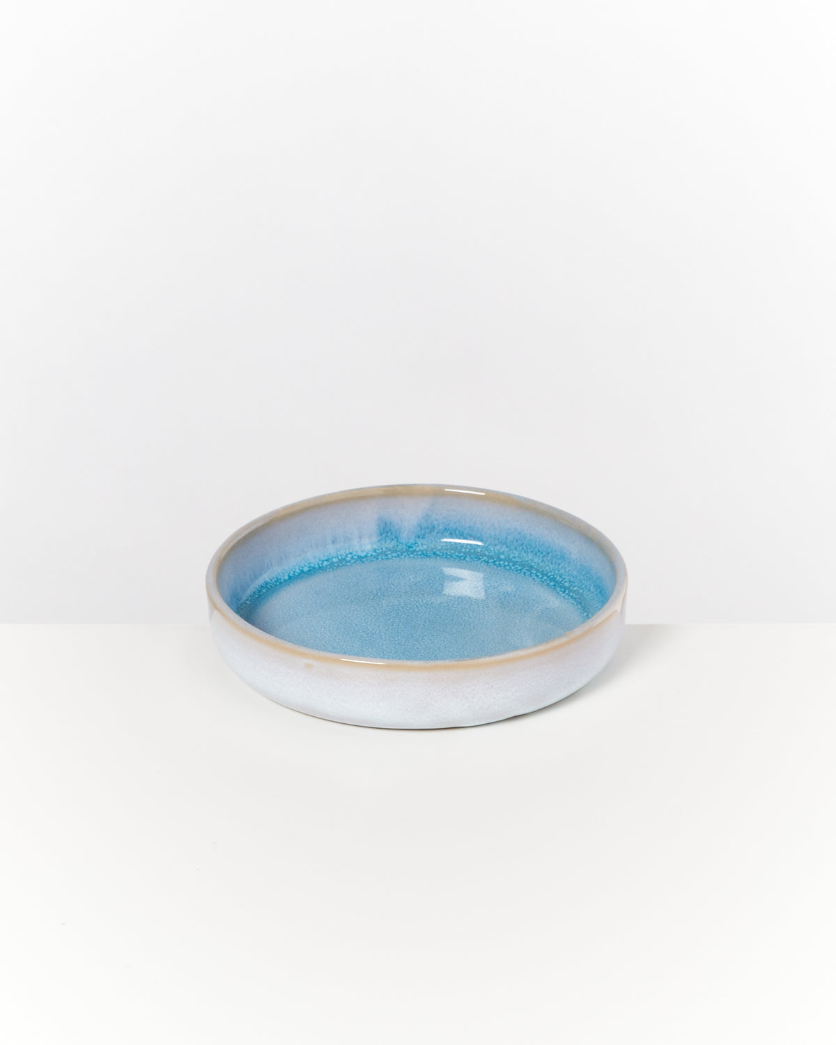 Flache, runde, blau glasierte Keramikschale auf weißem Hintergrund.