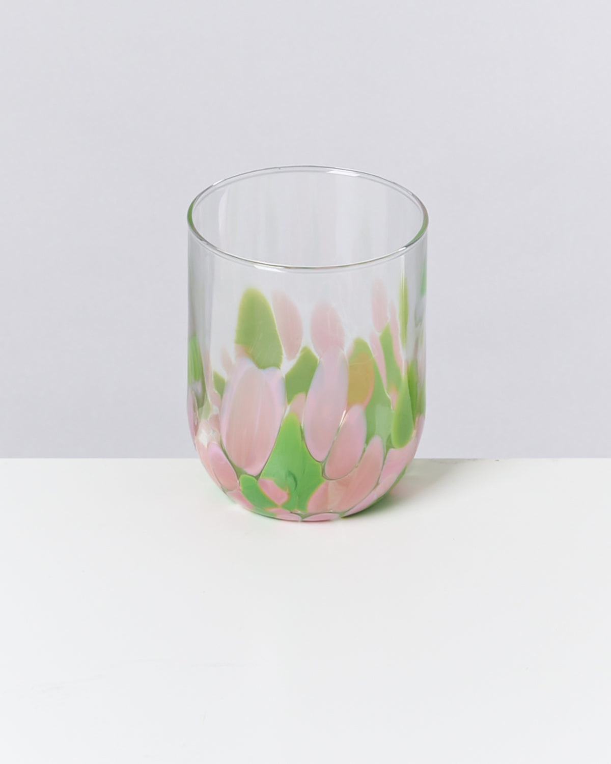 Ein Glas mit rosa und grünen Tupfen auf hellem Untergrund.