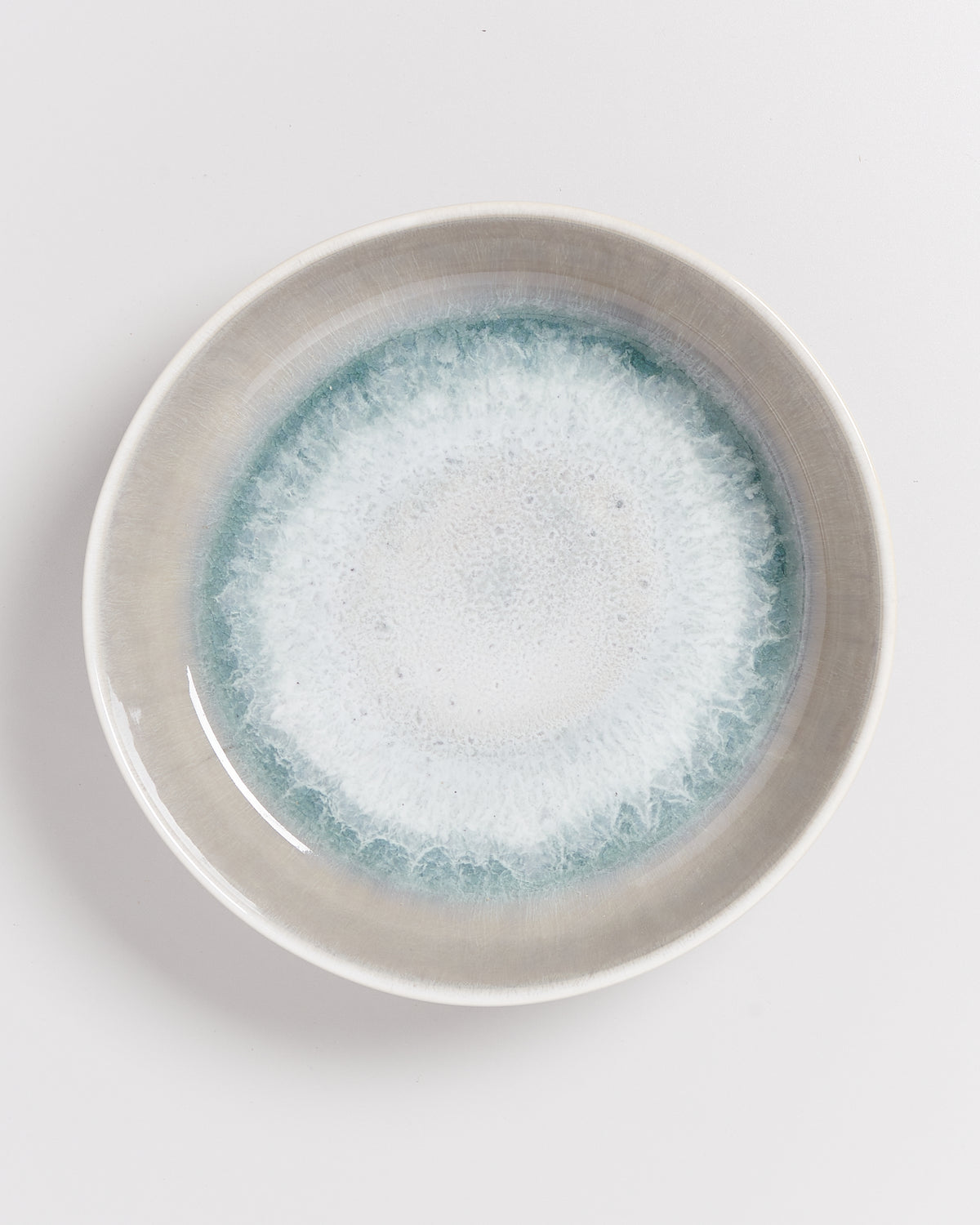 Keramikteller mit blau-weißer Glasur, die einen wasserähnlichen Effekt erzeugt, auf weißem Hintergrund.