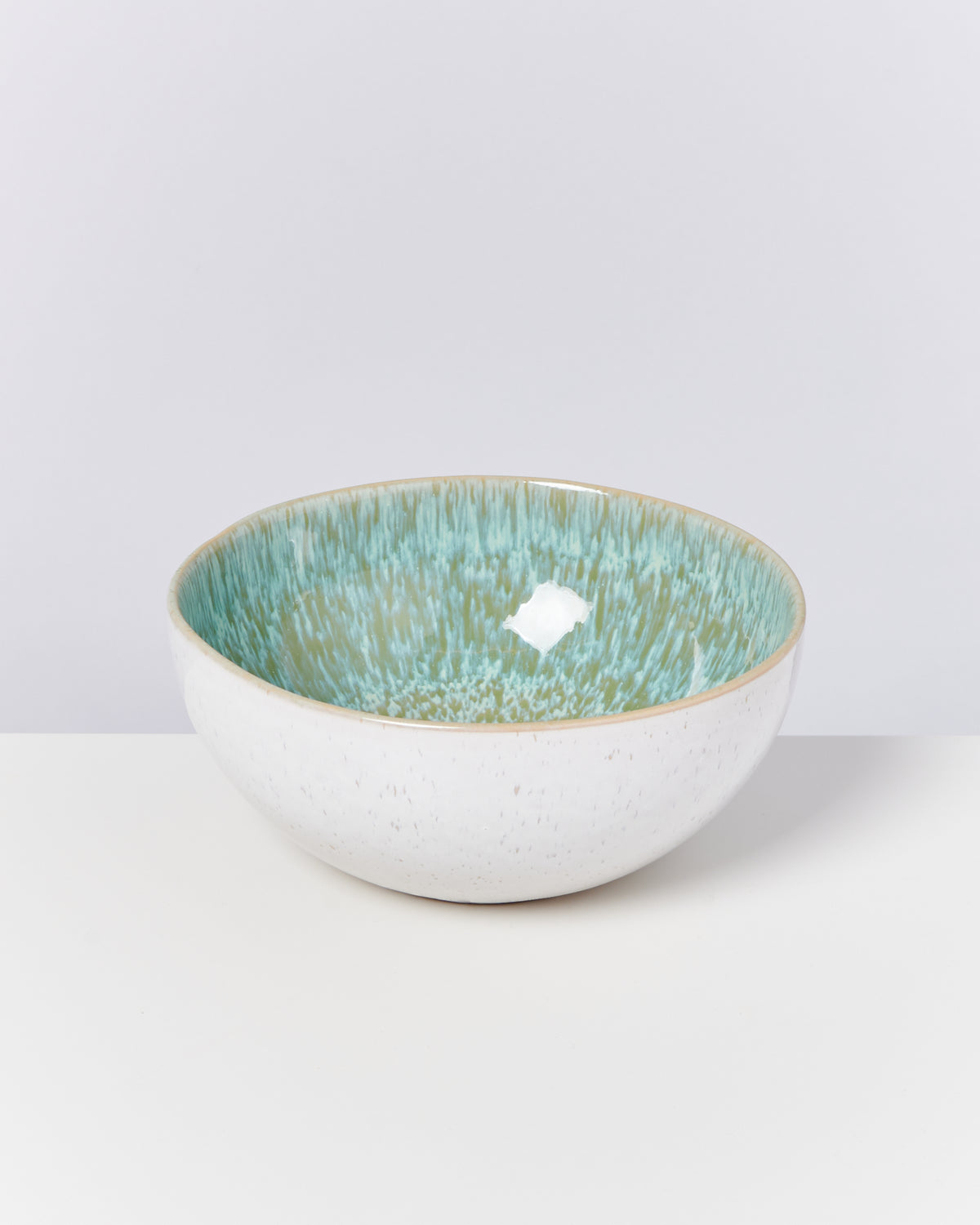Weiße Schale mit grün-blauem Innendesign auf einem weißen Hintergrund.