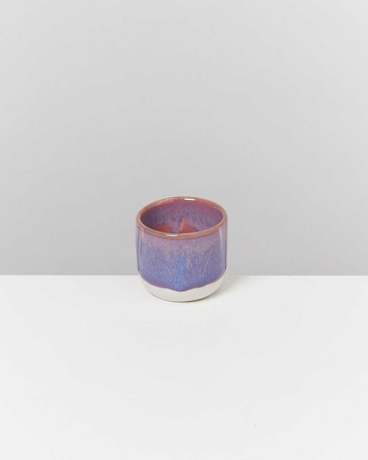 Keramikbecher mit violett-blauer Glasur auf weißem Hintergrund.