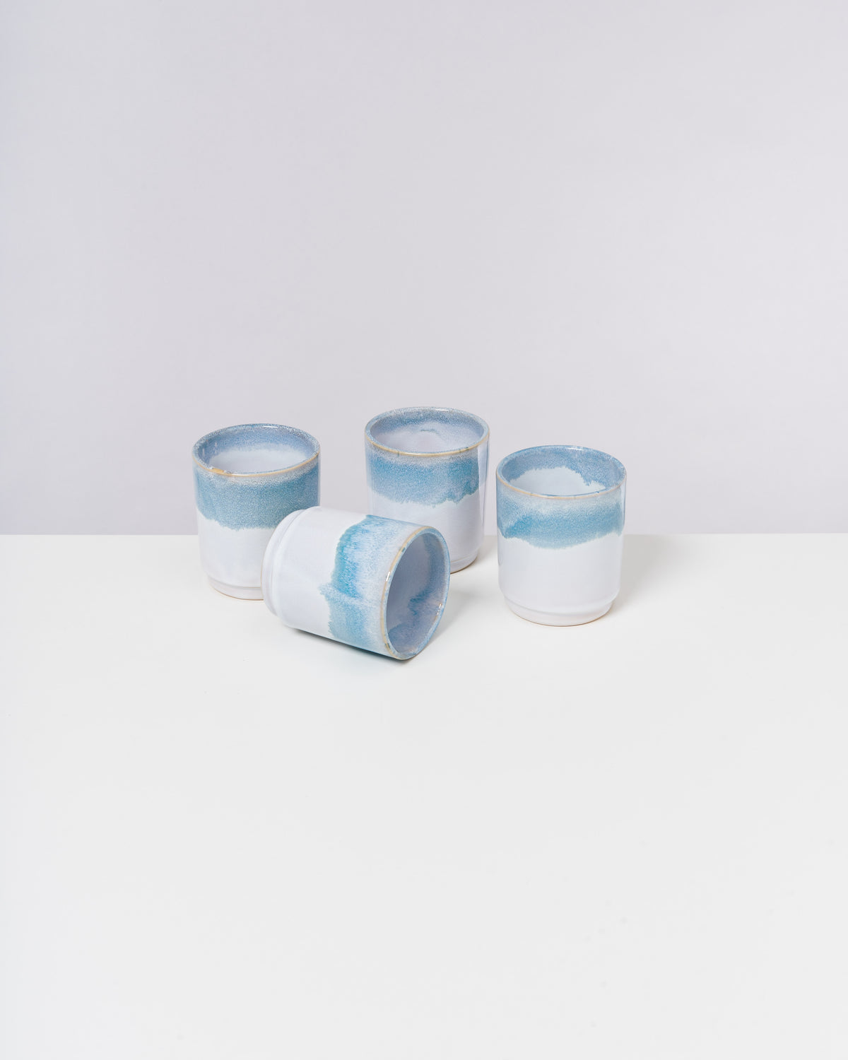 Vier weiß-blaue Keramikbecher stehen auf einem weißen Tisch, einer liegt seitlich.