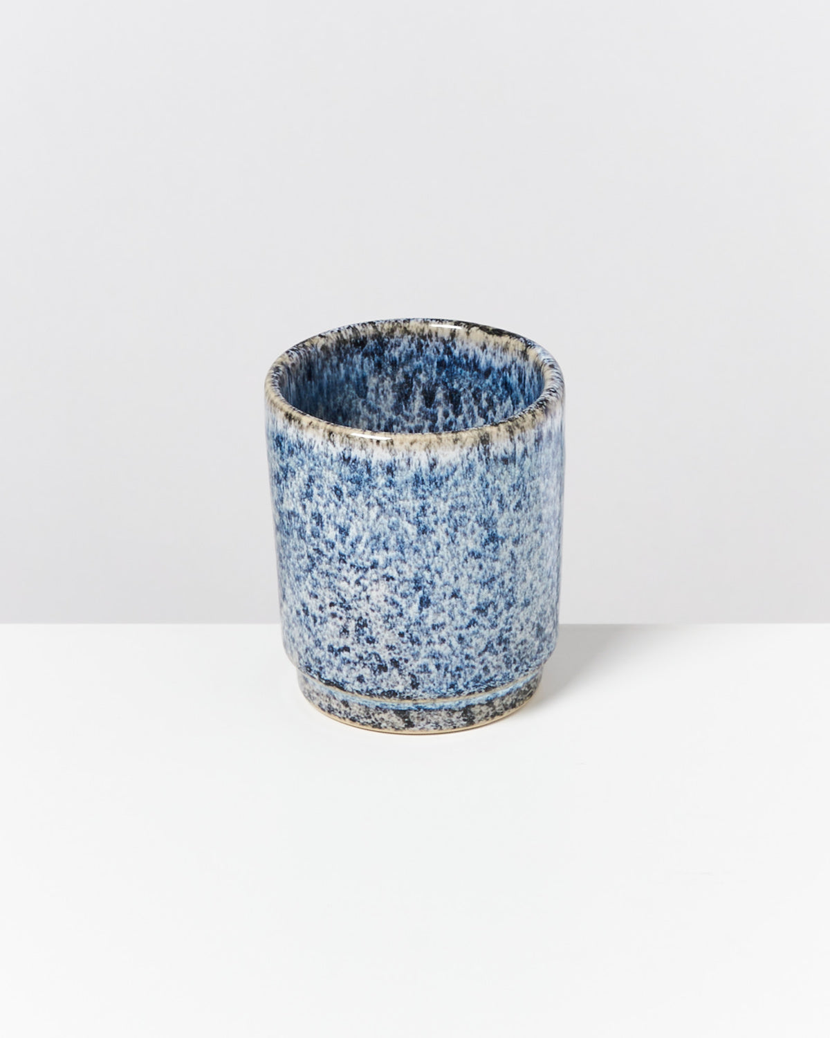Blau-weiß gesprenkelter Keramikbecher auf einem weißen Hintergrund.