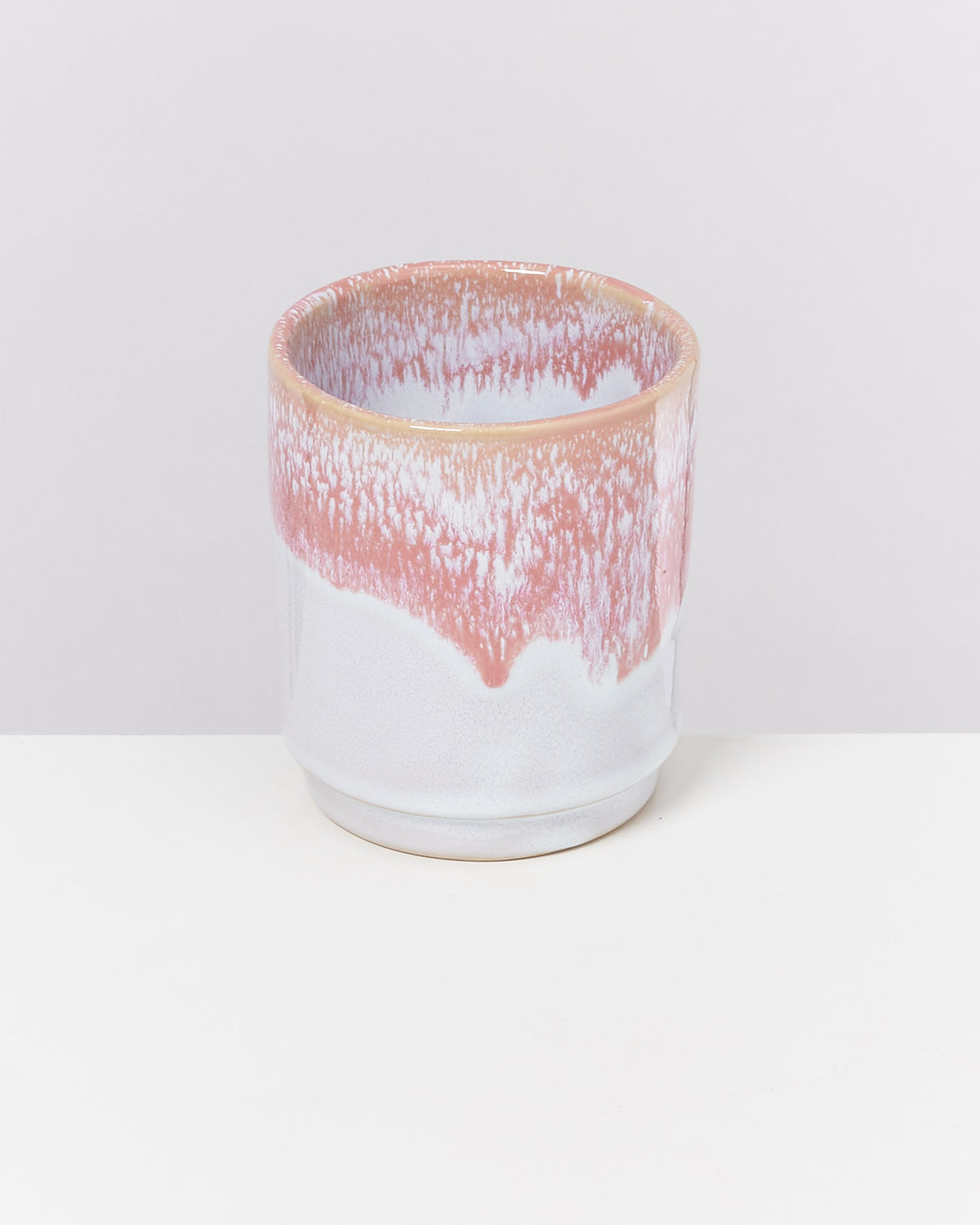 Keramikbecher mit weißer und rosa glasierter Oberfläche auf hellem Hintergrund.