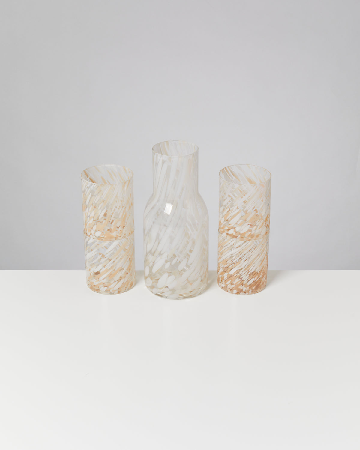 Drei Glasbehälter mit marmorierter Textur in Weiß und Beige auf einem weißen Tisch vor neutralem Hintergrund.