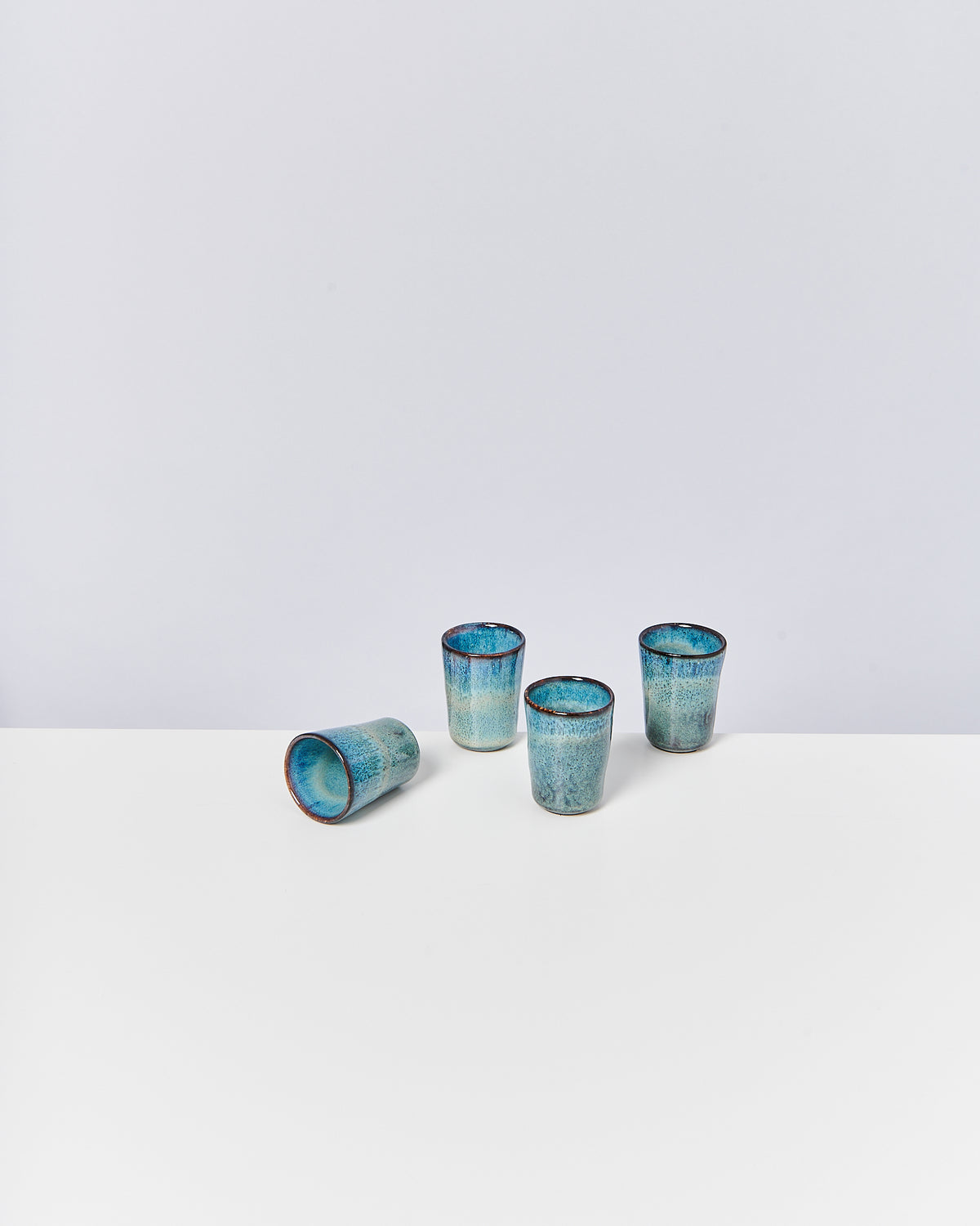 Vier blaue Becher aus Keramik stehen auf einem weißen Tisch, einer liegt auf der Seite.