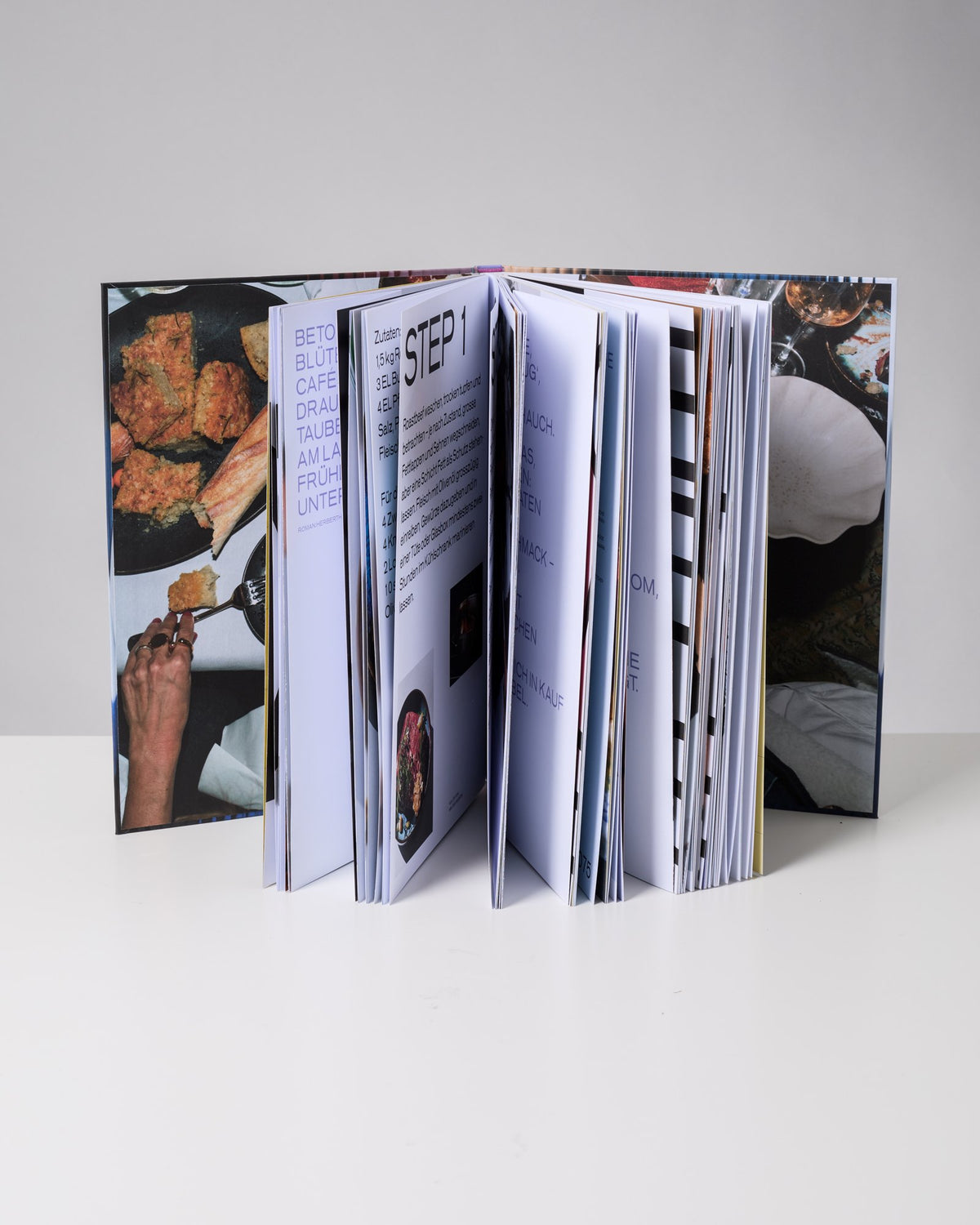Ein geöffnetes Buch mit Rezepten und Fotos liegt auf einem weißen Tisch.