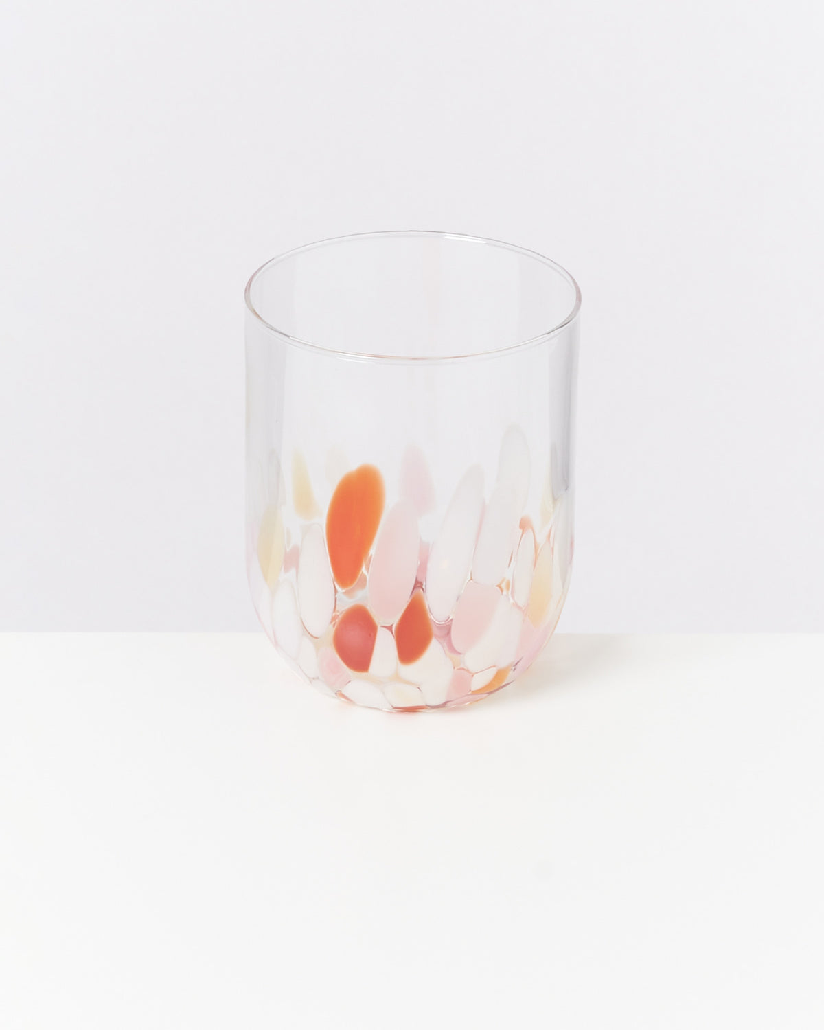 Ein Glas mit bunten, ovalen Farbflecken auf einem weißen Hintergrund.