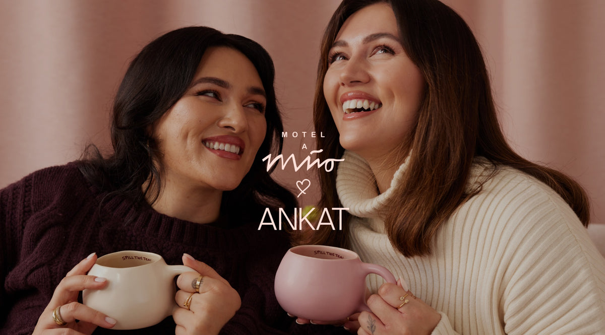 Zwei lachende Frauen halten Tassen in den Händen, vor einem rosa Hintergrund mit der Aufschrift "Motel a Mio ♥ ANKAT".