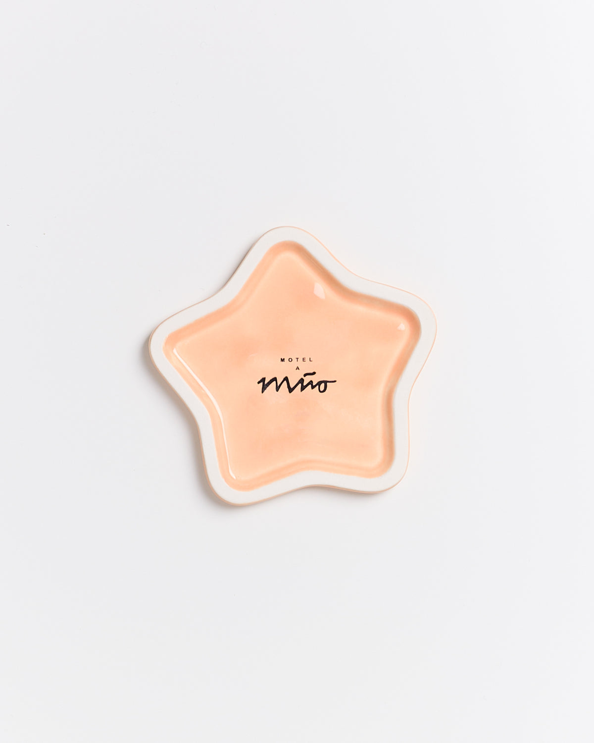 Sternförmiger, orangefarbener Teller mit dem Aufdruck "Motel a Miio" in einem minimalistischen Design auf weißem Hintergrund.