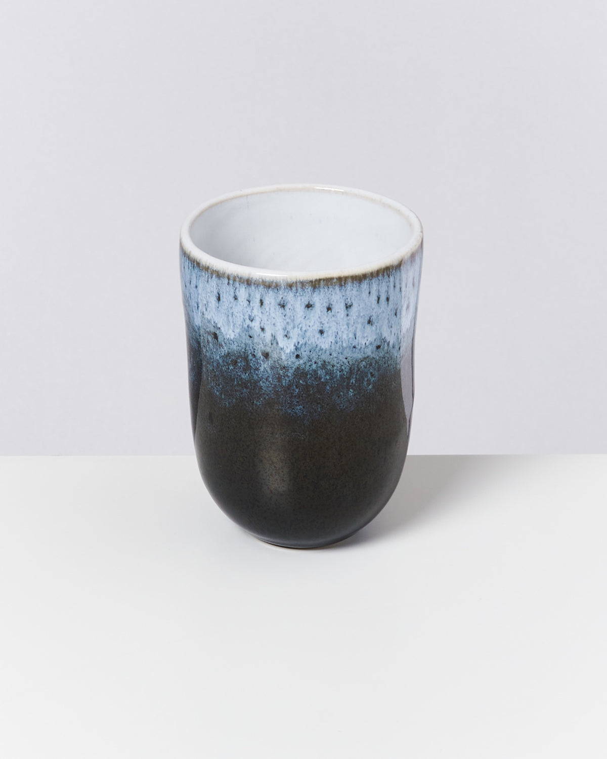 Keramikbecher mit blau-schwarzer Glasur auf weißem Hintergrund.