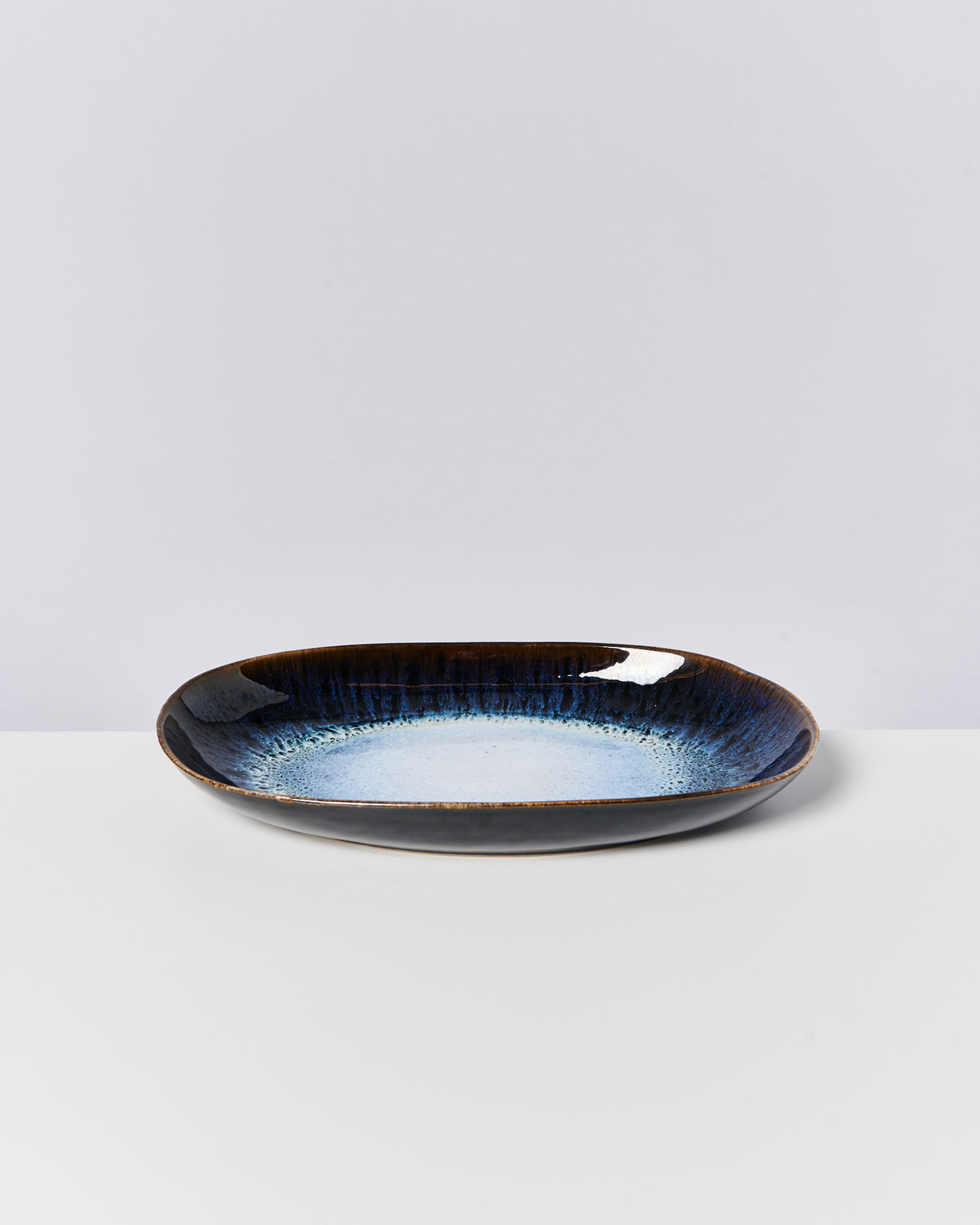 Ovale Keramikschale mit blau-schwarzer Glasur auf weißem Hintergrund.
