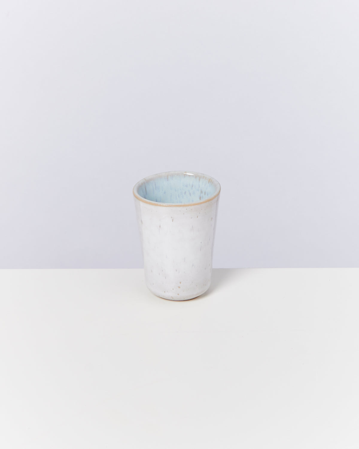 Weißer Keramikbecher mit blauer Innenseite, auf hellem Hintergrund platziert.