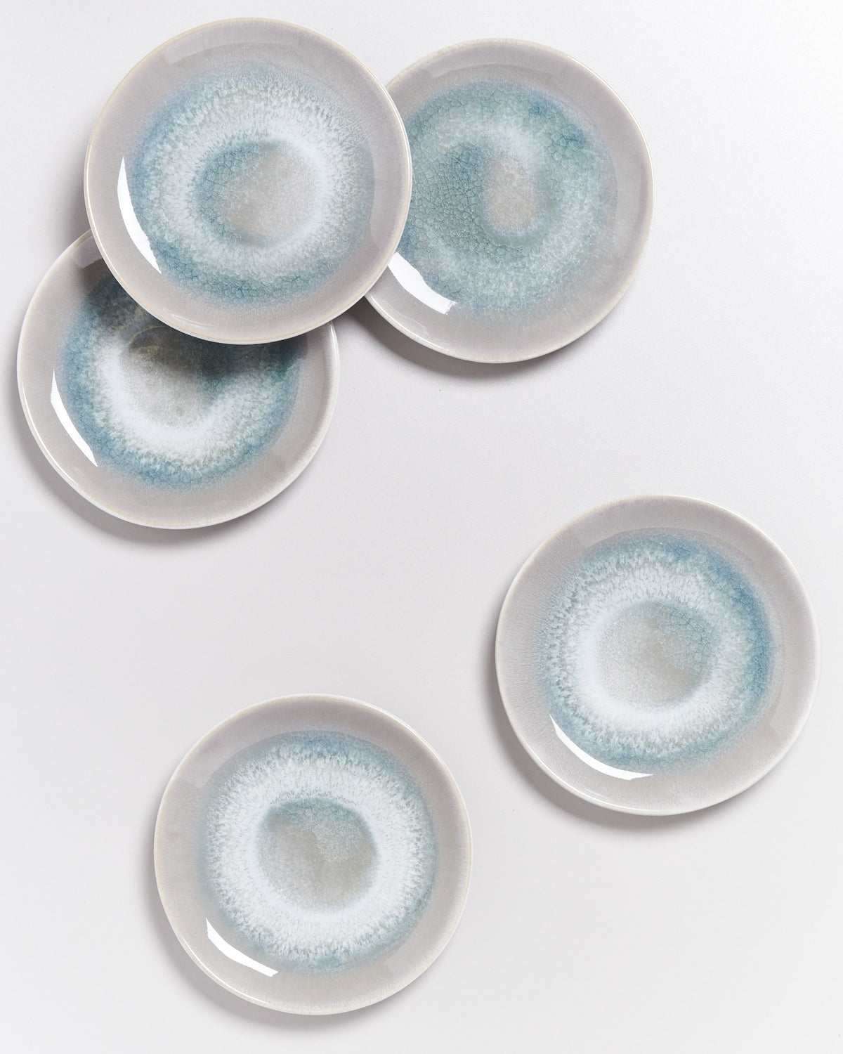 Fünf runde Teller mit blau-grauem, kreisförmigem Muster liegen auf weißem Hintergrund.