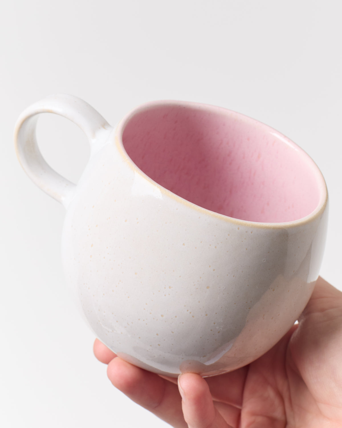 Eine Hand hält eine weiße Tasse mit rosa Innenseite vor einem hellen Hintergrund.