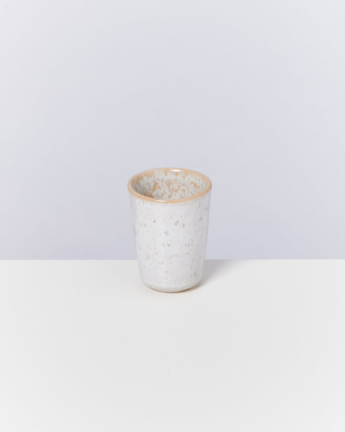 Weiße, gesprenkelte Keramiktasse auf einem Tisch vor neutralem Hintergrund.