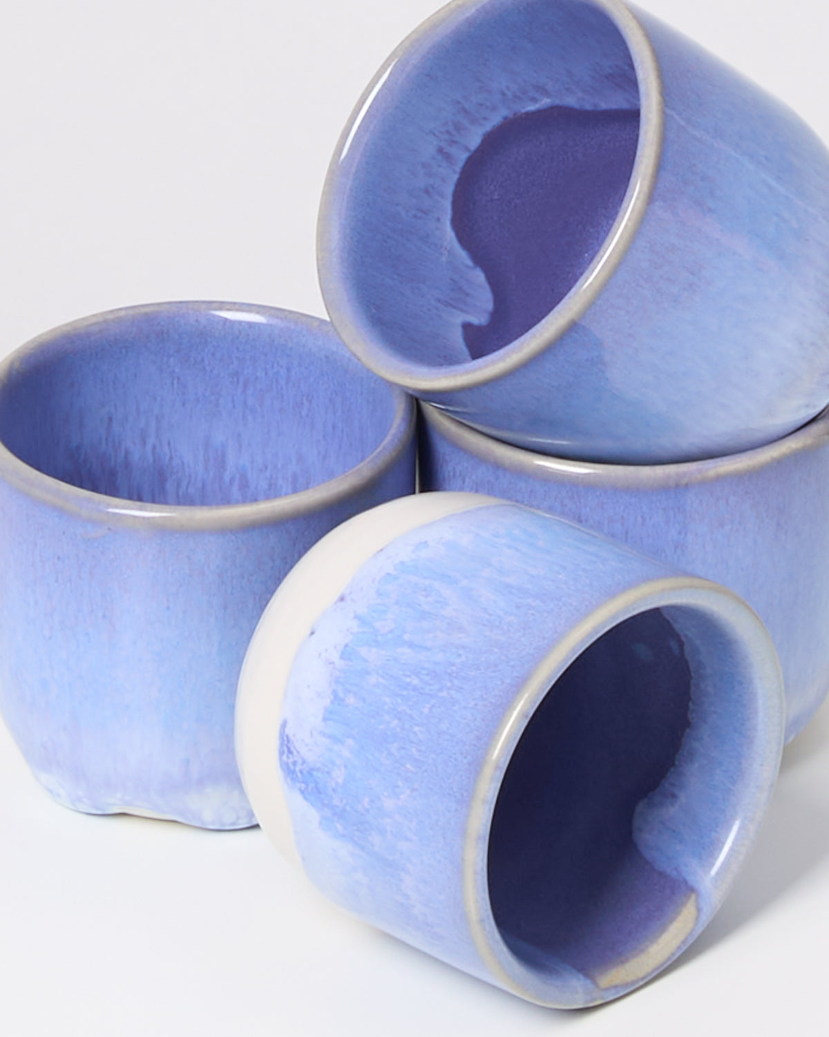Vier stapelbare, blaue Keramikbecher mit glänzender Oberfläche auf einem weißen Hintergrund.