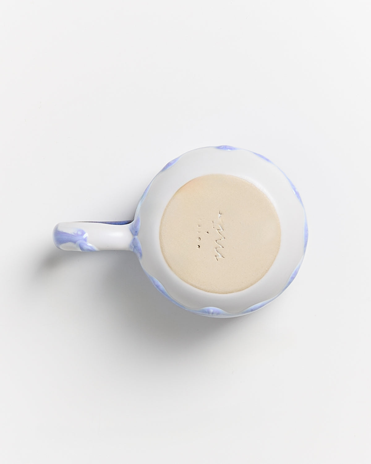 Unterseite einer Tasse mit blau-weißem Muster und Henkel, auf hellem Hintergrund.