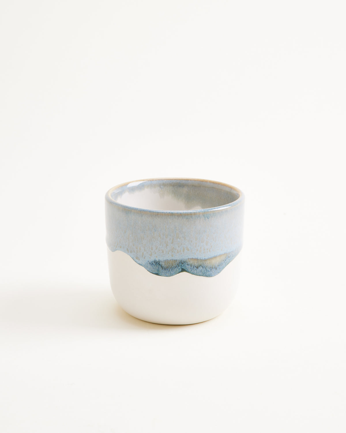 Keramikbecher mit blau-weißer Glasur auf weißem Hintergrund.