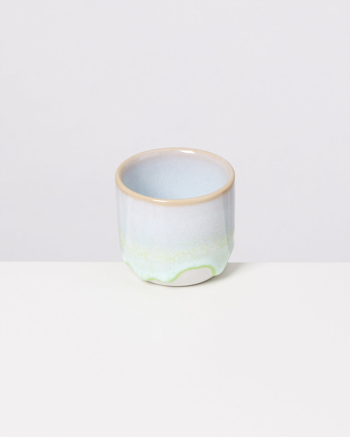 Keramikbecher mit heller blauer und grüner Glasur auf weißem Hintergrund.