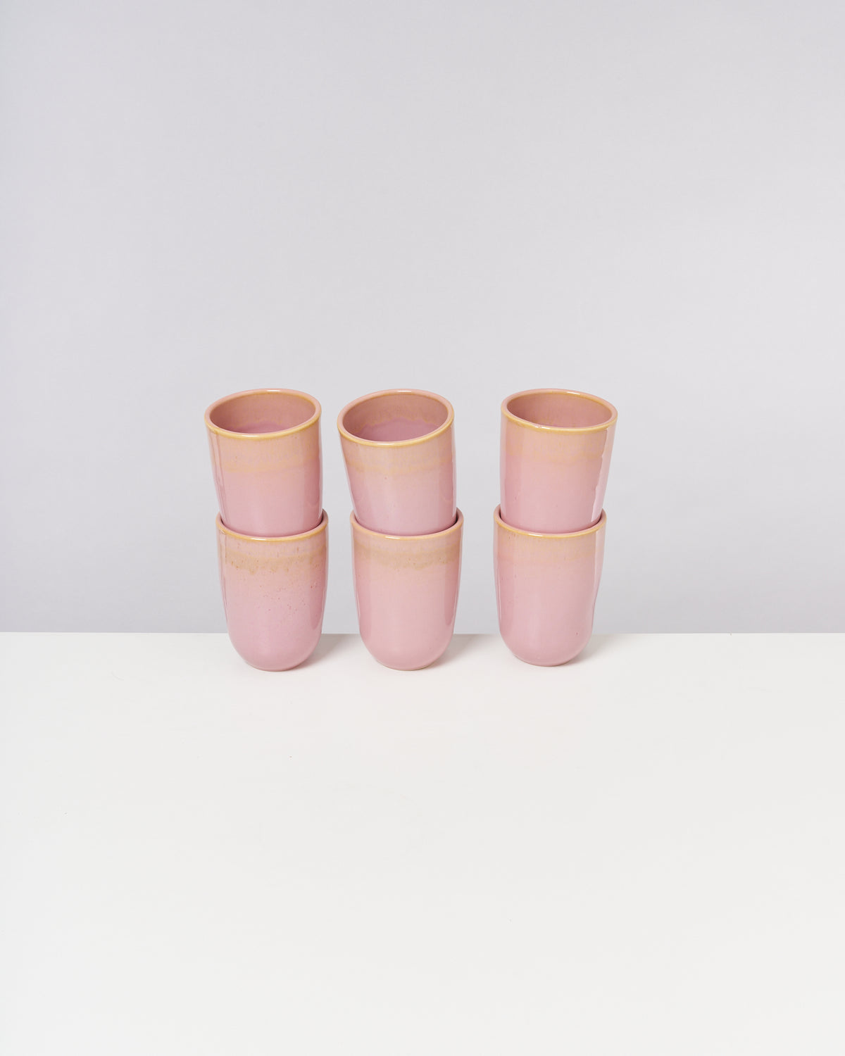 Sechs gestapelte rosa Becher aus Keramik auf einem weißen Tisch vor neutralem Hintergrund.