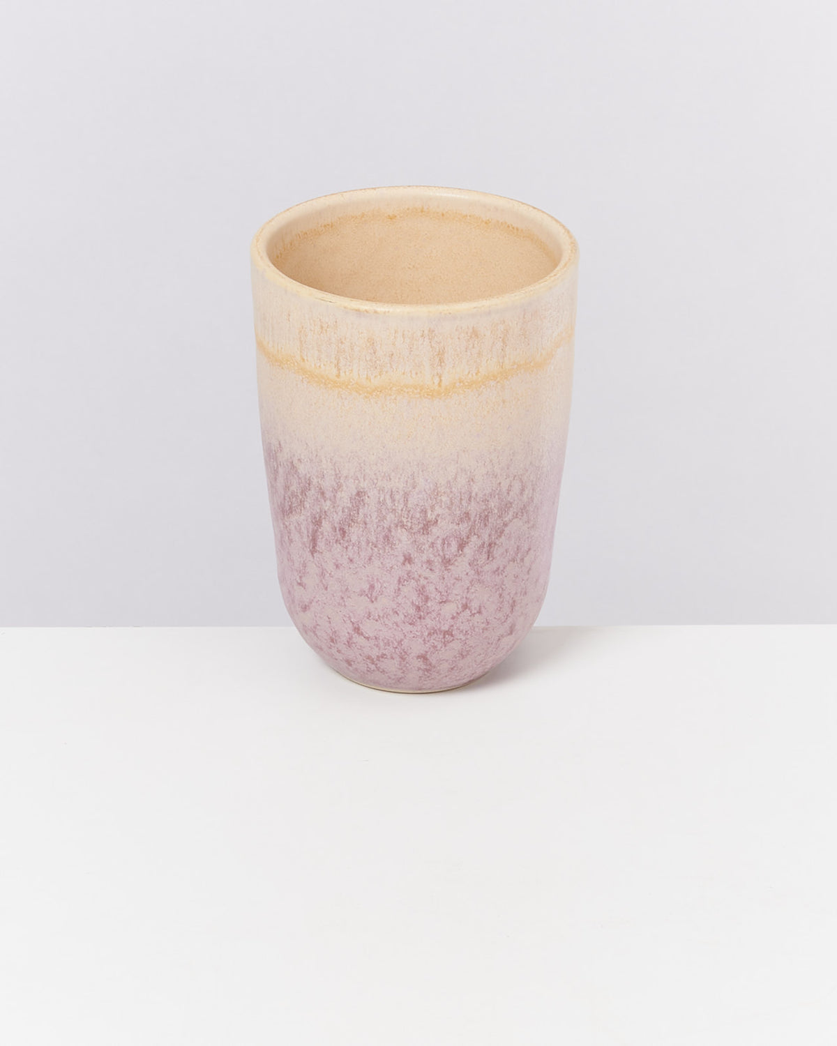 Becher mit grauer und rosa Ombre-Glasur steht auf weißem Untergrund vor einem hellgrauen Hintergrund.