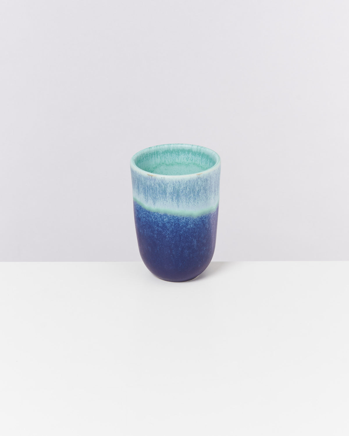 Blauer und grüner Keramikbecher auf weißem Hintergrund.