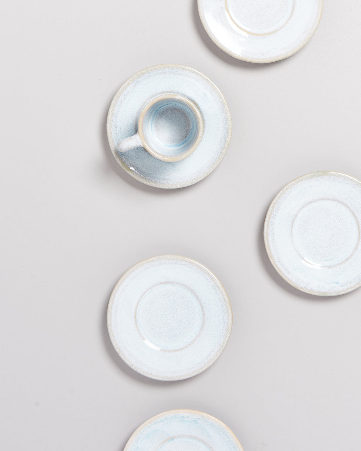 Fünf hellblaue Untertassen und eine passende Tasse auf einem hellgrauen Hintergrund arrangiert.