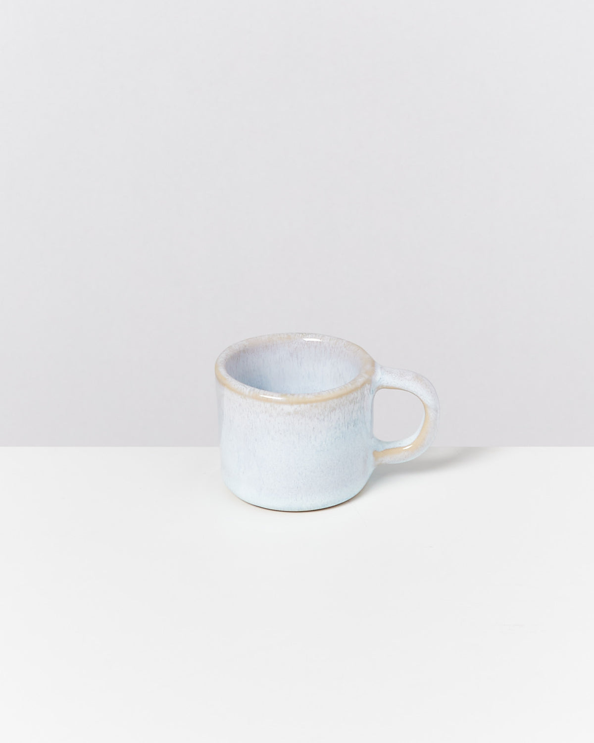 Eine hellblaue Keramiktasse mit Henkel steht auf einem weißen Tisch vor einem grauen Hintergrund.