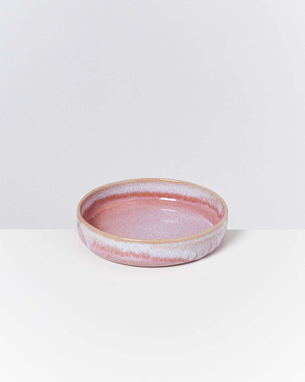 Runde, flache, rosa Keramikschale mit weißem Rand auf weißem Hintergrund.
