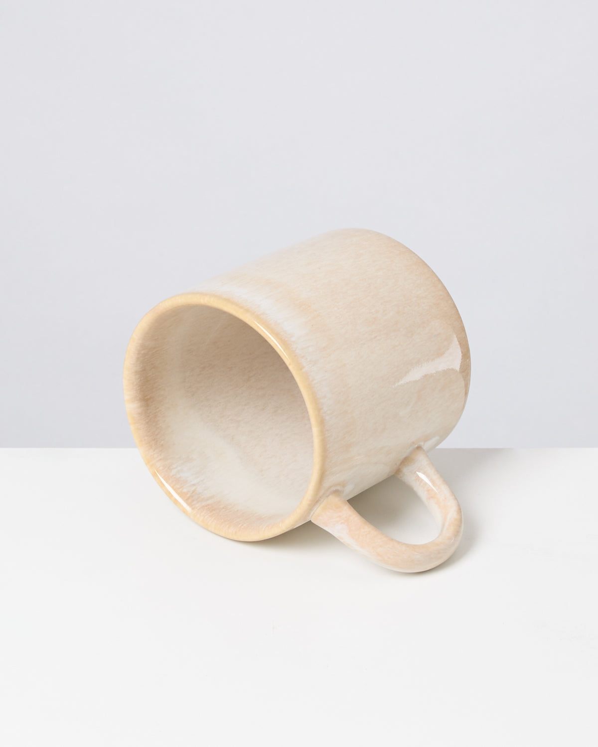 Beige Tasse liegt auf der Seite auf einer weißen Oberfläche, vor einem grauen Hintergrund.