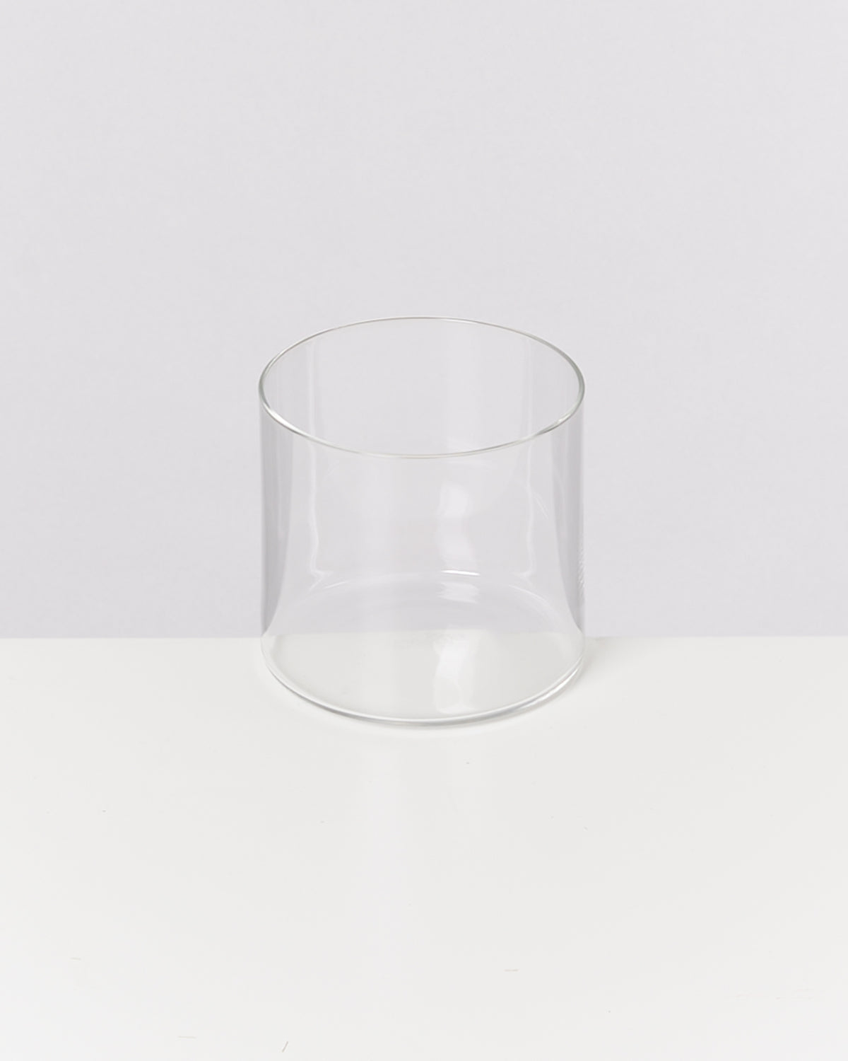 Ein transparentes, leeres Glas steht auf einer weißen Oberfläche vor einem neutralen Hintergrund.