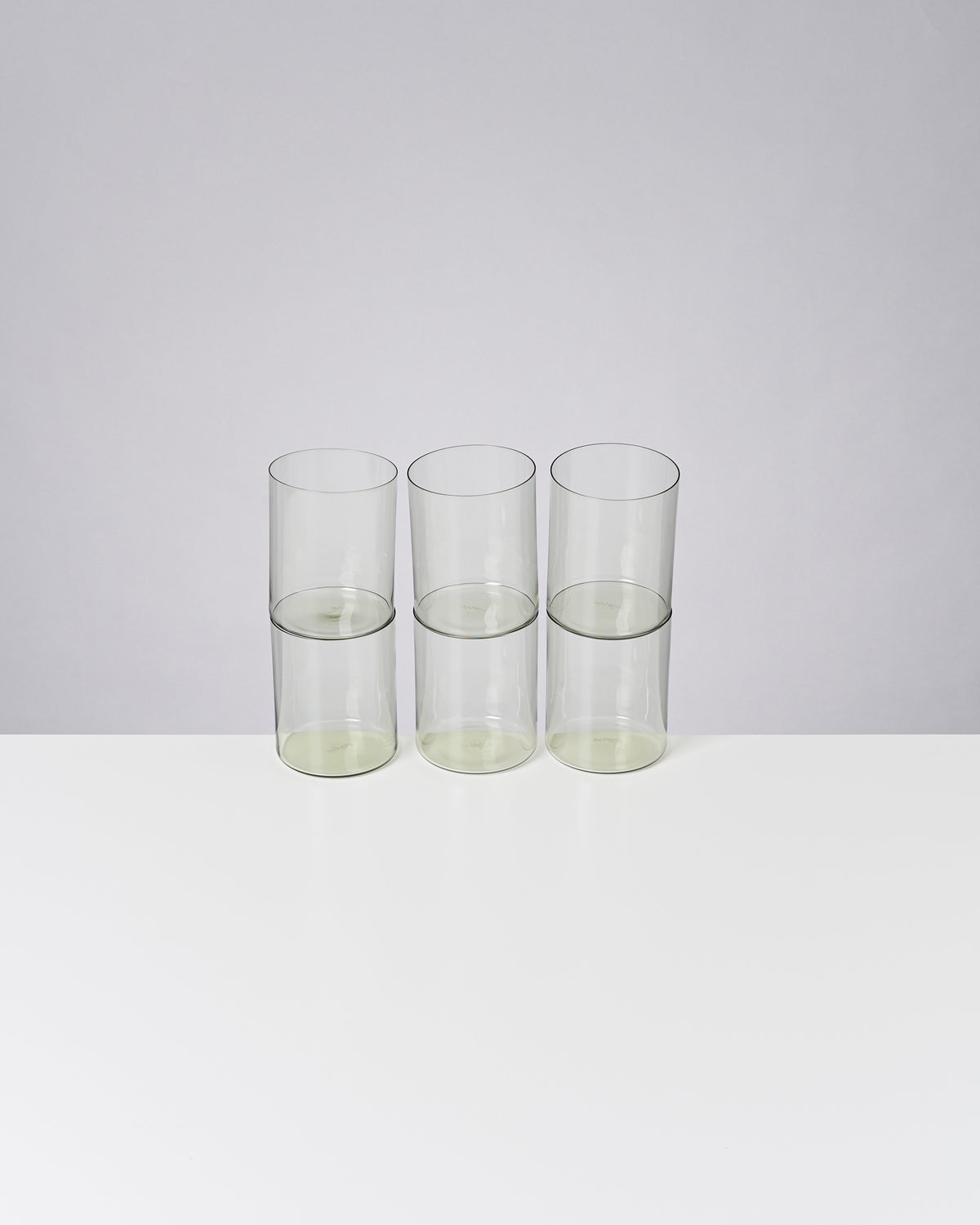 Drei transparente Gläser stehen nebeneinander auf einem weißen Tisch vor einem grauen Hintergrund.