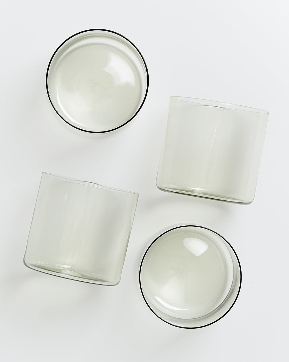 Vier durchsichtige Glasbecher liegen von oben fotografiert auf einer weißen Oberfläche.