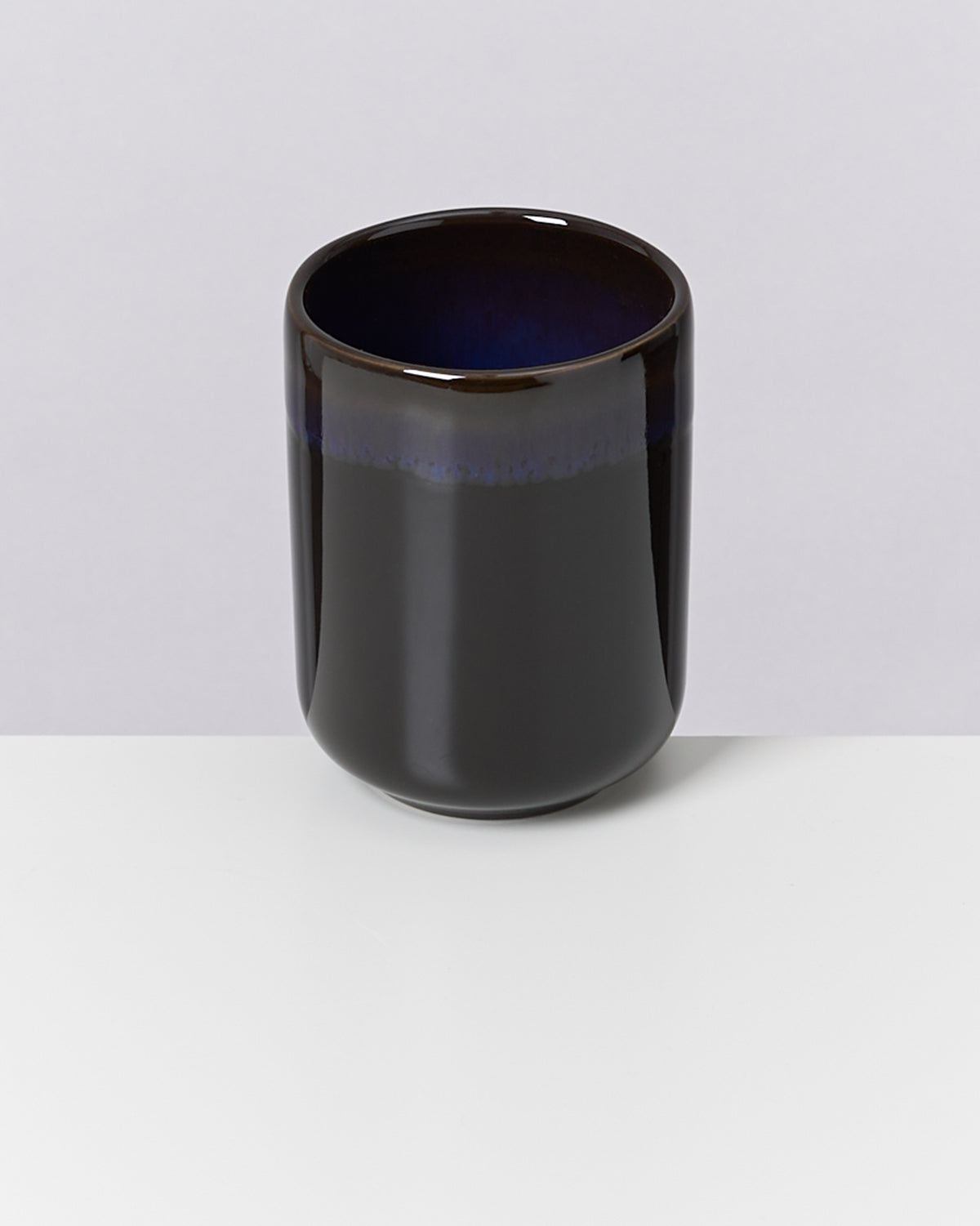 Schwarze, glänzende Keramiktasse mit einem dunkelblauen Rand auf einem weißen Hintergrund.