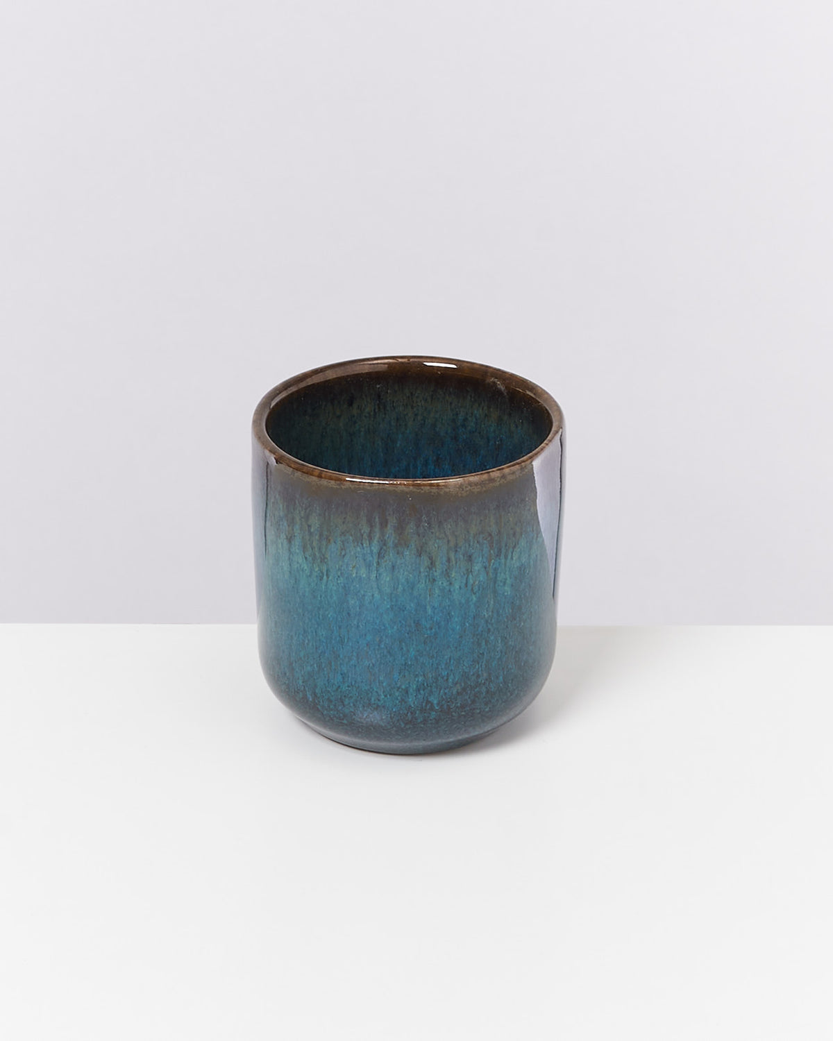 Blauer Keramikbecher mit braunem Rand auf weißem Hintergrund.
