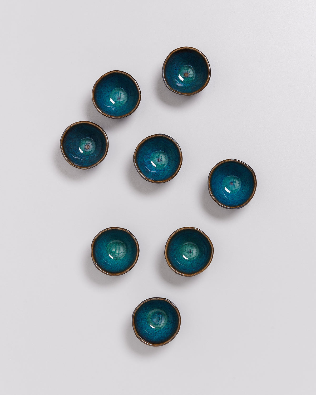Acht kleine Schalen mit blauer Glasur sind auf einem weißen Untergrund angeordnet.
