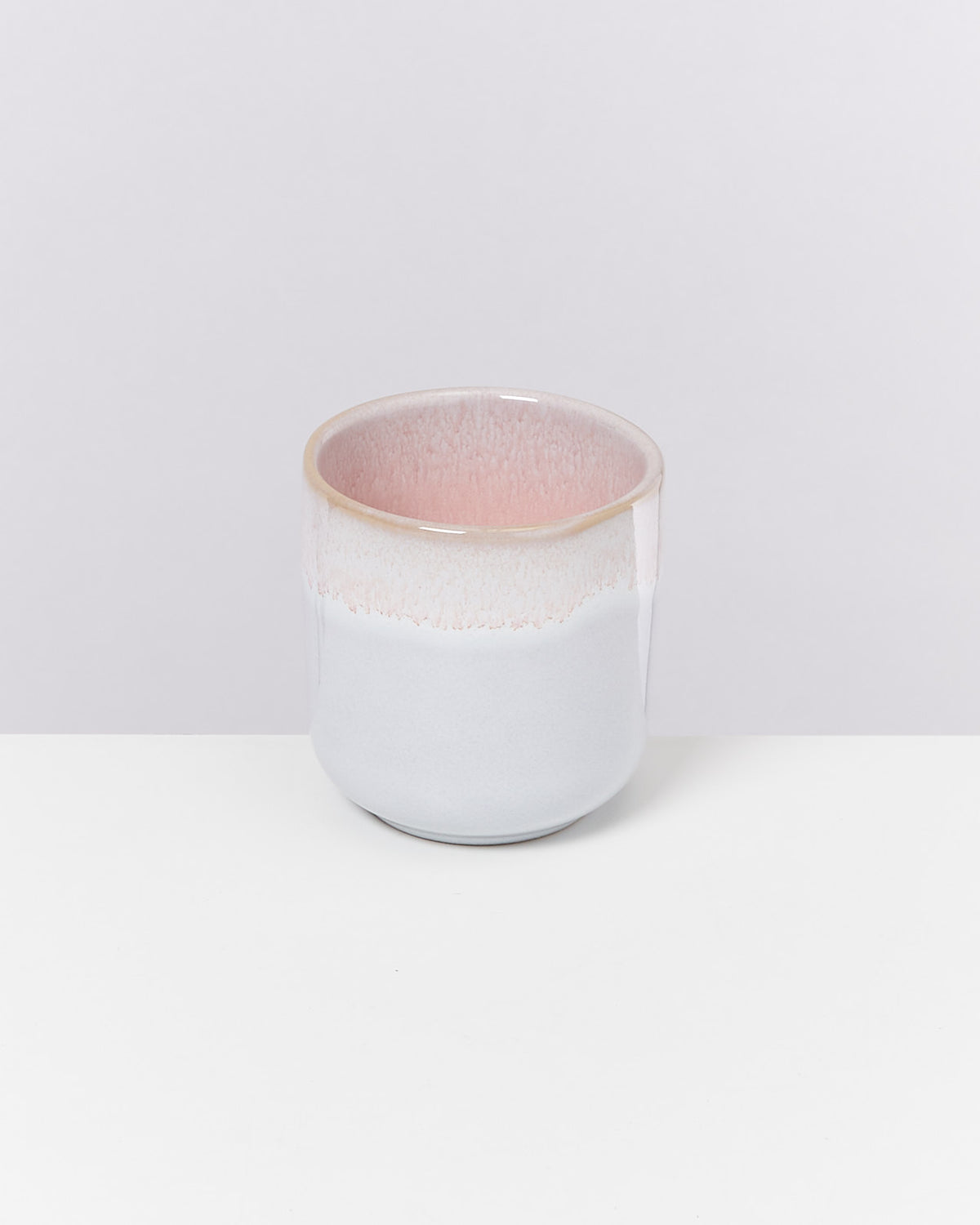 Keramikbecher mit einem Farbverlauf von rosa oben nach weiß unten, auf weißem Hintergrund.