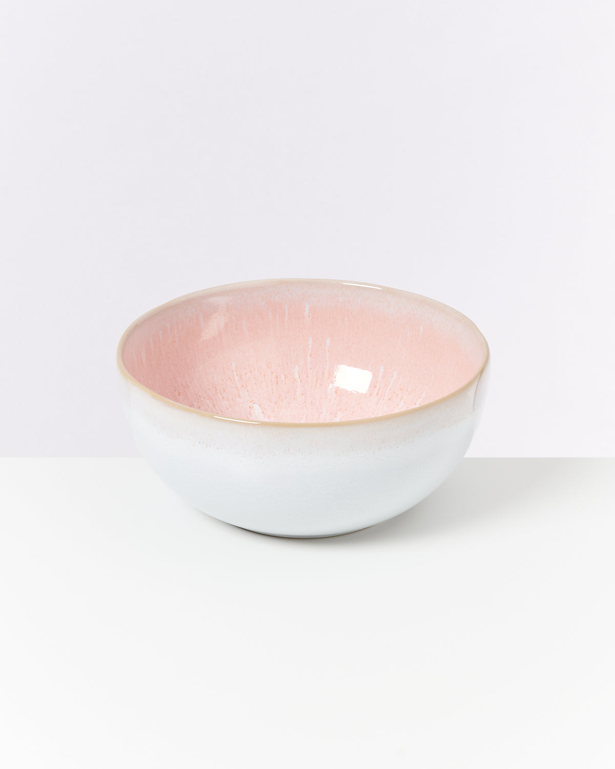 Keramikschüssel mit rosa Innenseite und weißer Außenseite steht auf einem weißen Hintergrund.