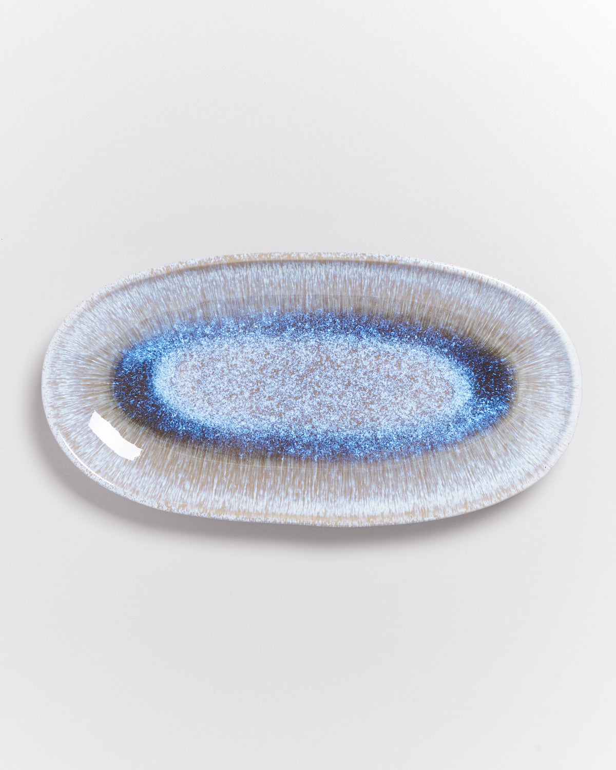 Ovaler Teller mit blauem und beigem Muster auf weißem Hintergrund.