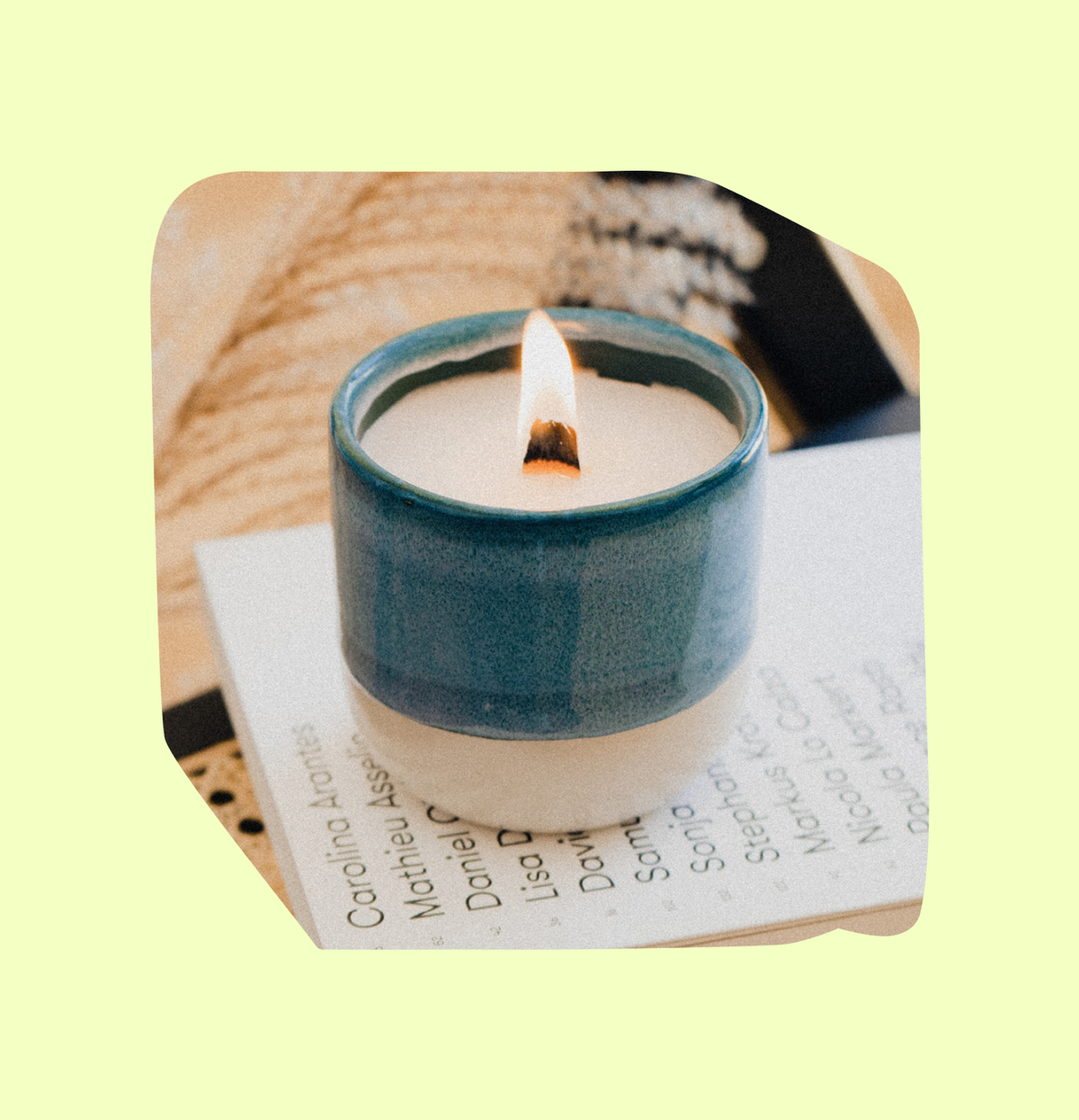 Brennende Kerze in blauer Keramikschale auf Büchern vor hellem Hintergrund.