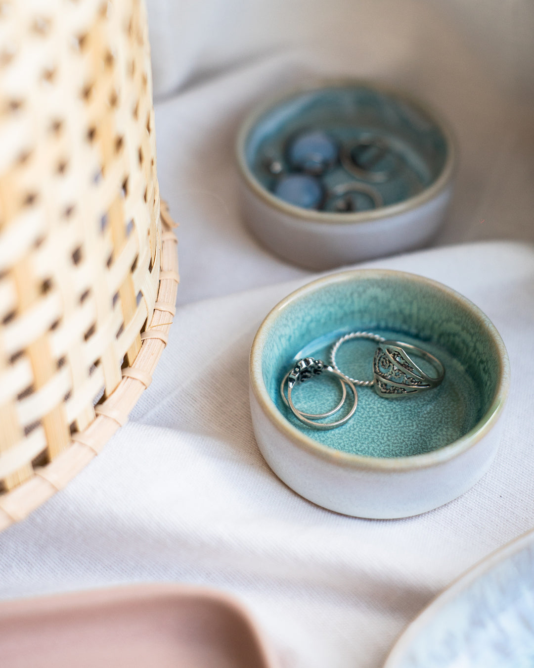 Kleine, blaue Schalen mit silbernen Ringen auf einem weißen Tuch, neben einem geflochtenen Korb.