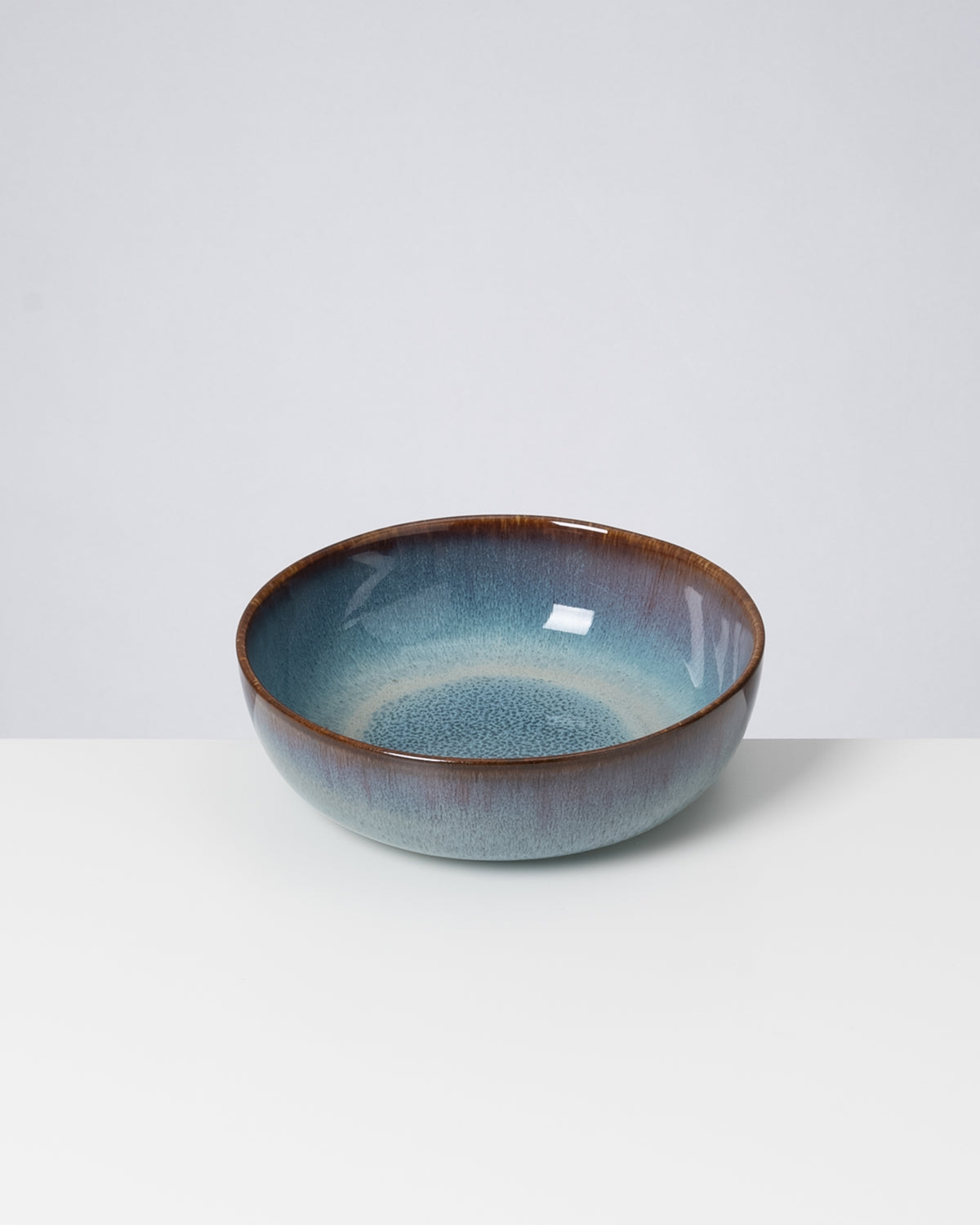 Keramikschale mit blau-brauner Glasur auf weißem Untergrund.