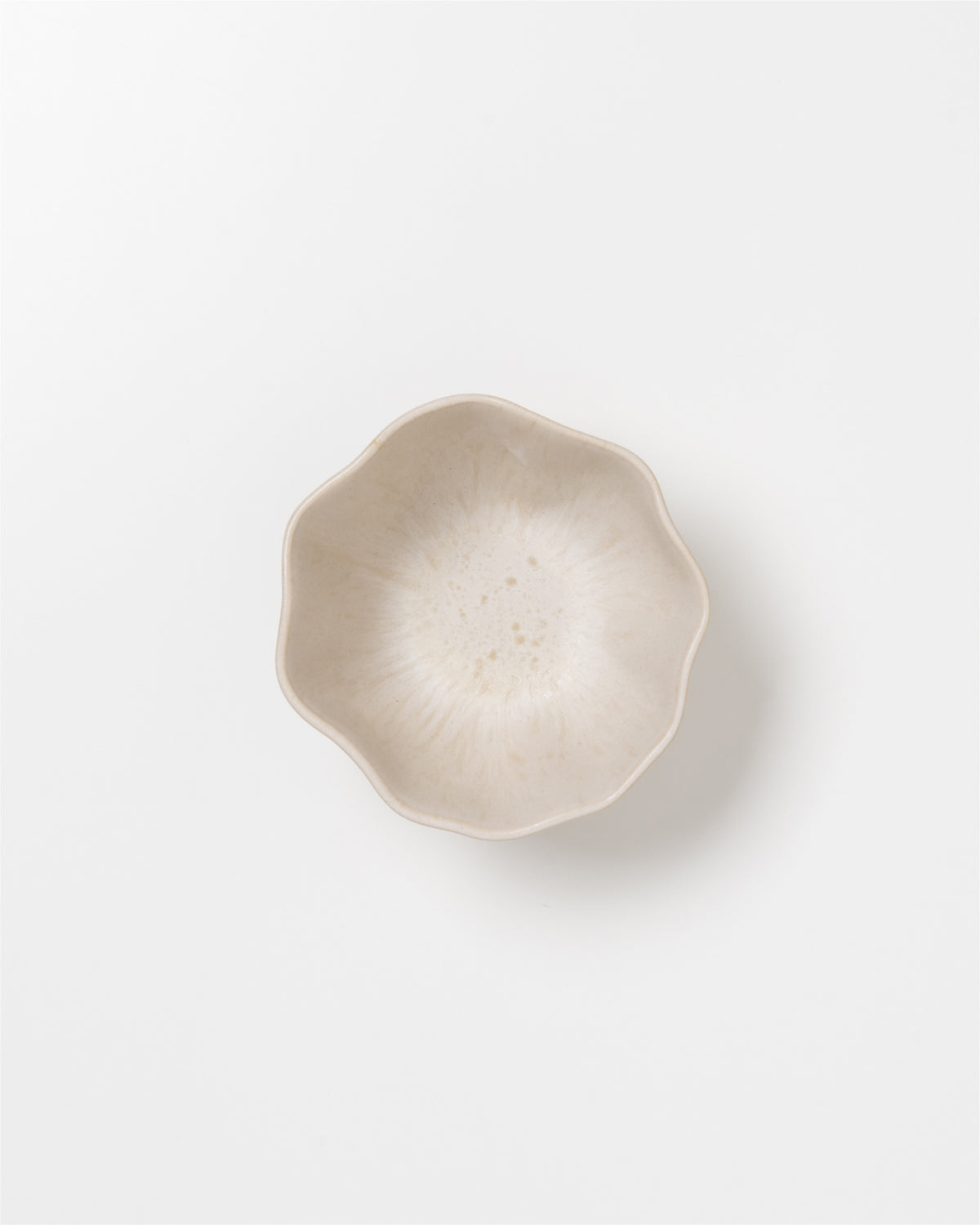 Beige, blütenförmige Schale auf weißem Hintergrund.